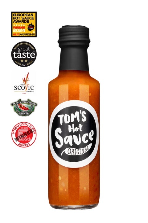 Eine Flasche von Tom’s Hot Sauce Original steht vor einem weißen Hintergrund und präsentiert ihre leuchtend orange Farbe sowie mehrere preisgekrönte Auszeichnungen.